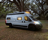 A silver campervan with lights on, parked under large, mossy trees at dusk. Ideal for your next rv rental adventure.