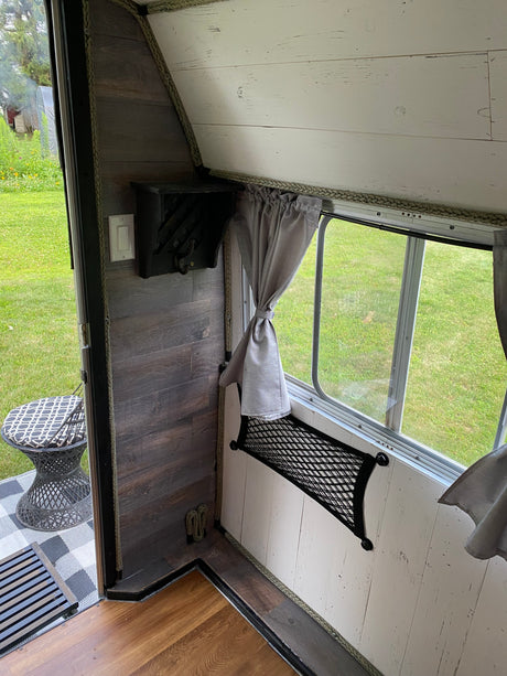 Cozy RV rental interior showing wood walls, a window with curtains, and integrated storage, overlooking a green yard.