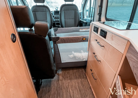 This rv rental interior features a baby playpen with a baby, front seats, and kitchenette, perfect for family road trips.