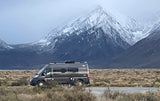Gray RV rental parked on a vast plain with dramatic snow-capped mountains. Ideal for scenic road trips and wilderness adventures.
