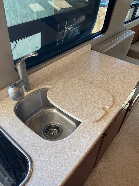 RV rental kitchen: Stainless steel sink, faucet, speckled beige countertop with a cover, and window view in a modern RV.