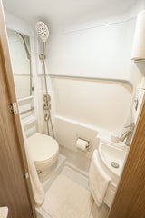 This RV rental wet bath features a white toilet, compact sink, and handheld shower for efficient use of space.
