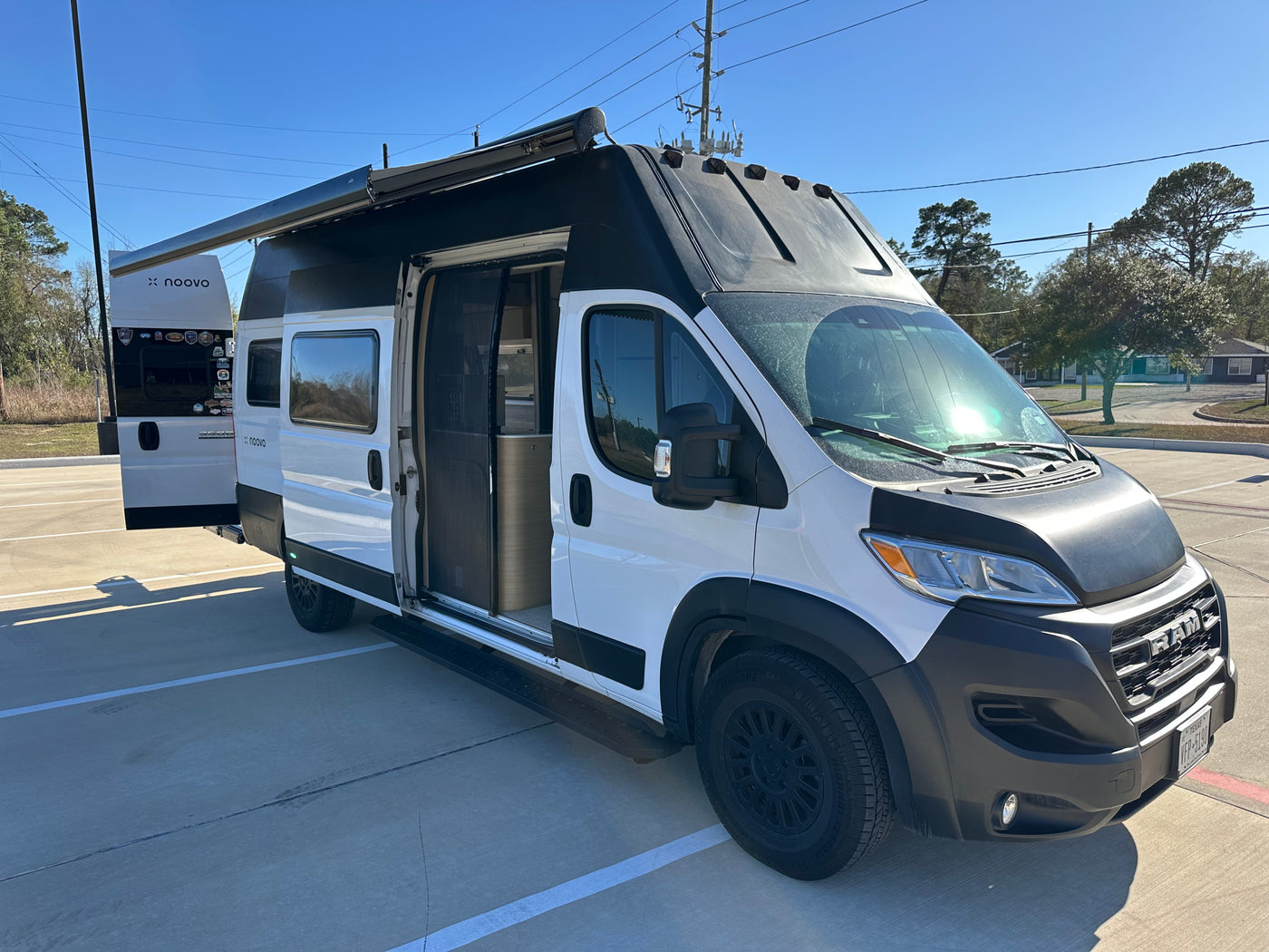 This white and black Noovo rv rental camper van with open doors and extended awning is ready for adventure. — photo 4