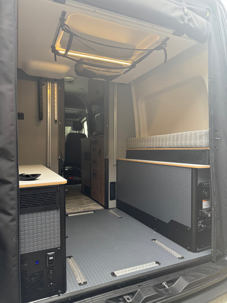 Spacious RV rental interior with bed, storage, and utility panels, offering functional mobile living for adventurers.