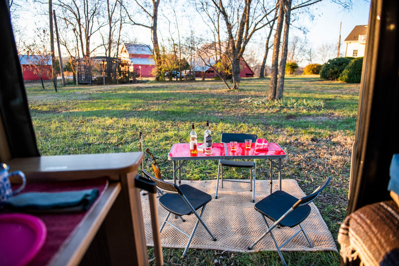 RV rental view: Relaxing outdoor setup with a table, chairs, drinks, and a violin at sunset in a grassy field. — photo 13