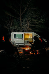 Night scene: Friends gathered around a bright campfire with a guitar, next to a cozy rv rental camper van.
