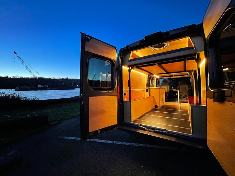 Experience van life! This custom camper van RV rental interior glows at dusk, parked by a river with a distant crane. — photo 5