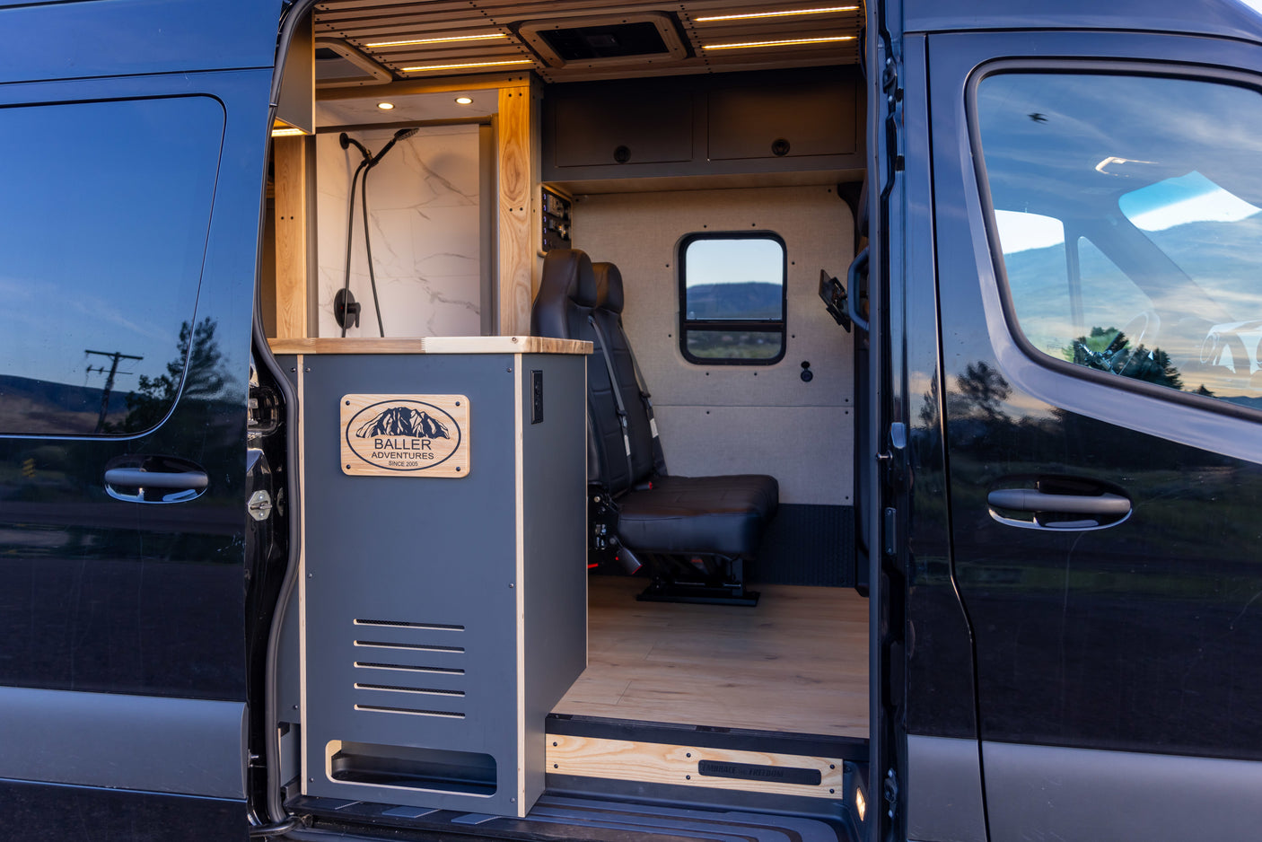 Custom Baller Adventures camper van RV rental interior: featuring a modern shower area, comfortable seating, and wood paneling.