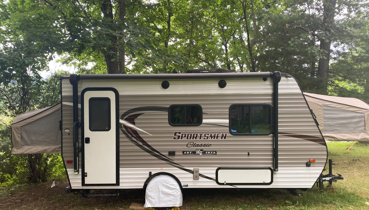 This Sportsmen Classic hybrid RV rental is set up for camping in a wooded area, with its tent-like bunks extended.