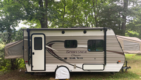 This Sportsmen Classic hybrid RV rental is set up for camping in a wooded area, with its tent-like bunks extended.