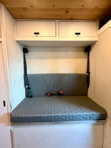 Cozy RV rental interior with a grey quilted bench seat, seatbelts, and overhead storage for comfortable travel.