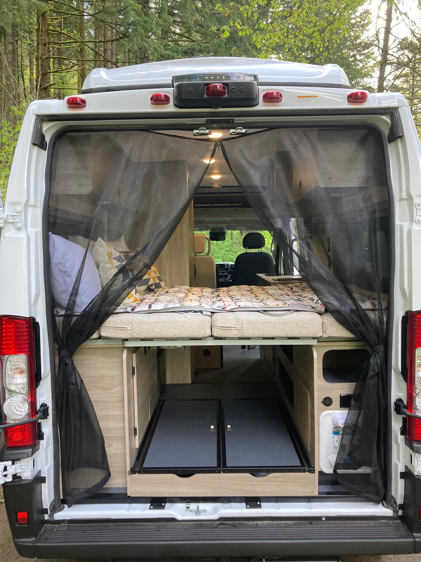 Explore this RV rental's spacious back: raised bed, pull-out storage, and bug screen for comfortable van life.