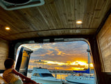 Enjoy a stunning marina sunset from this cozy RV rental! A child views boats from inside the wood-paneled camper van.