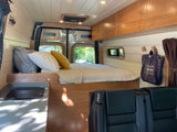 Modern RV rental interior featuring a comfortable bed, compact kitchen area, and rear passenger seats for travel.