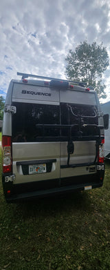 Back of a silver Thor Sequence **rv rental** with a bike rack, parked on grass. Florida license plate AV1 6RW is visible.