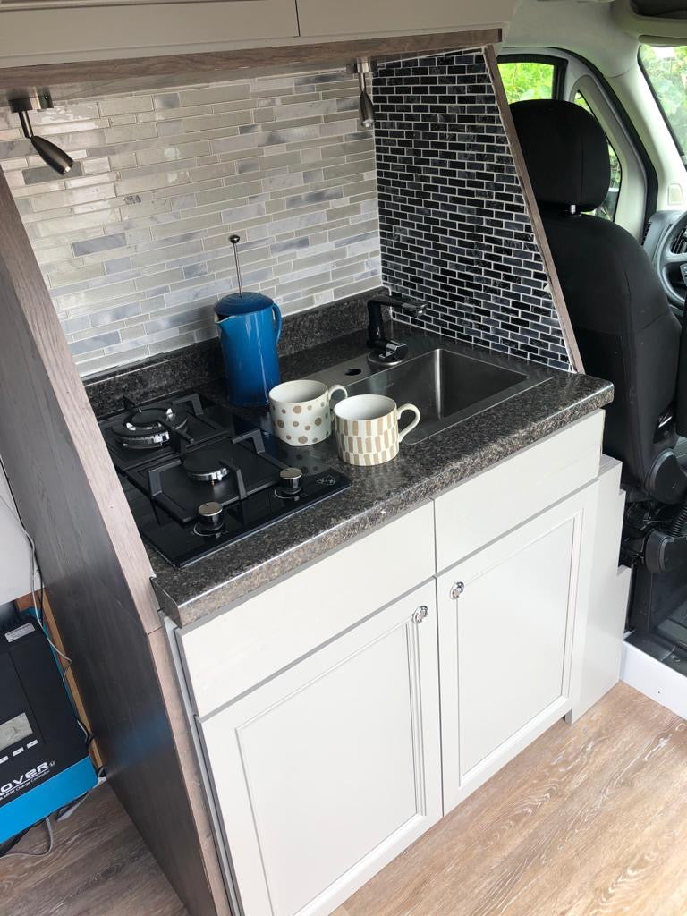 This compact RV rental kitchen features a sink, built-in stovetop, and white cabinets, perfect for on-the-go cooking.