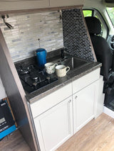 This compact RV rental kitchen features a sink, built-in stovetop, and white cabinets, perfect for on-the-go cooking.