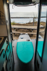 RV rental view: two surfboards ready for the beach from inside a camper van, overlooking the ocean and a picnic table.