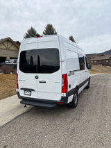 White Geotrek Sprinter RV rental van parked on a cloudy day, showing its rear and side with houses in the background.