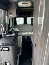 RV rental interior with sleek kitchen, gray bench seating, and smart controls visible, offering a comfortable space.