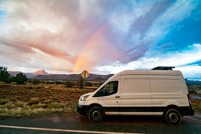  with vast desert mountains behind.|White rv rental camper van parked in a stunning red desert with layered rock formations under a clear blue sky.|White RV rental van parked in a vast white sand dune desert under a clear blue sky
