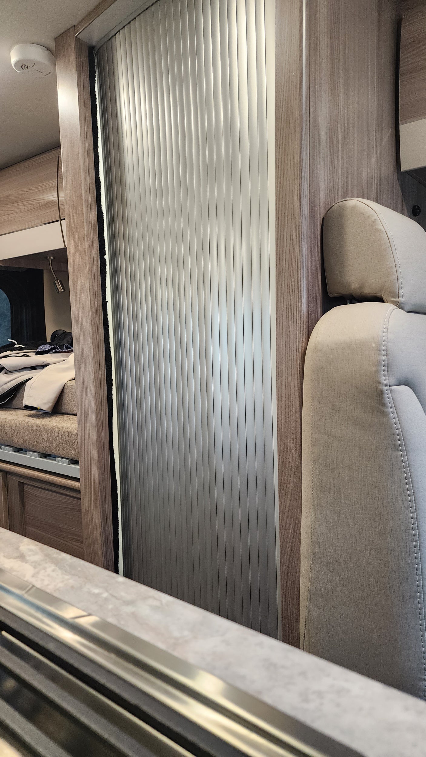 Upward view in an rv rental showing a comfortable bunk with beige upholstery, wood accents, and an aluminum roll-up window blind.