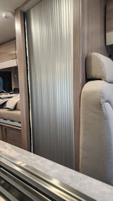 Upward view in an rv rental showing a comfortable bunk with beige upholstery, wood accents, and an aluminum roll-up window blind.