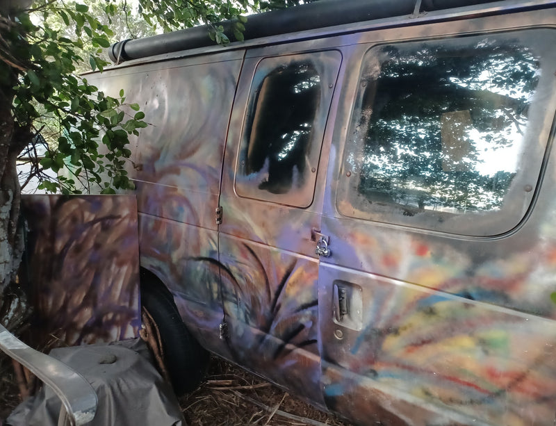 This vibrant, abstractly painted van could be a distinctive RV rental, parked outdoors with a roof rack & door lock. — photo 1