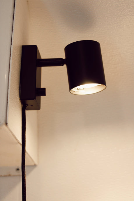 Compact black wall lamp providing warm light in an RV rental interior. Perfect for cozy reading nooks.