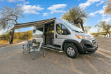 Silver camper van RV rental with awning extended and chairs set for outdoor leisure.