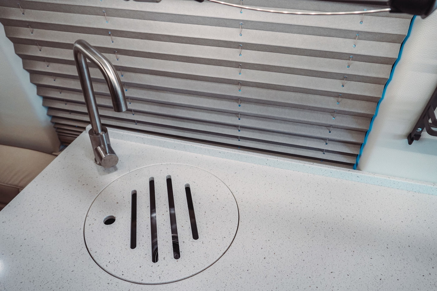 Modern RV rental interior featuring a white speckled countertop with a sleek stainless faucet and a unique slotted drain, next to pleated blinds. — photo 18