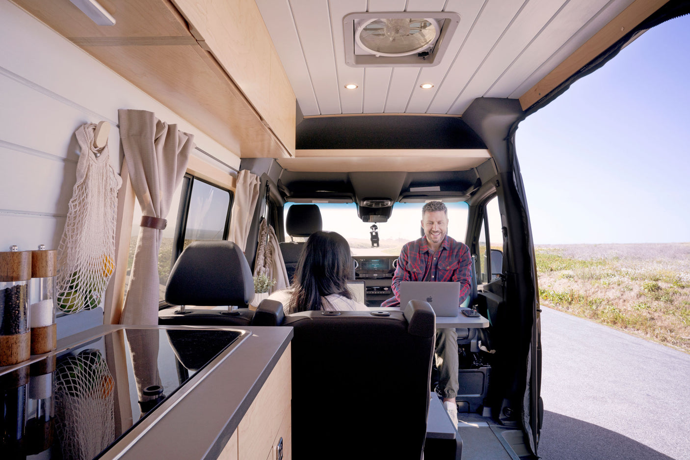 A man smiles while working on a laptop in a modern rv rental van. Enjoy mobile comfort & a roadside view.
