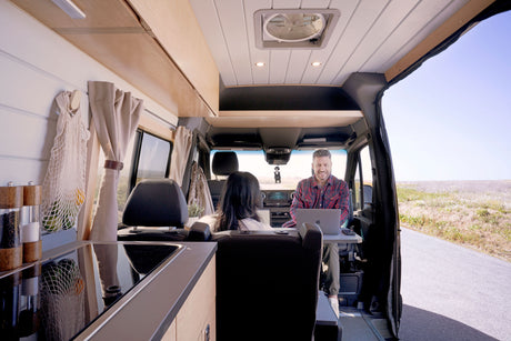 A man smiles while working on a laptop in a modern rv rental van. Enjoy mobile comfort & a roadside view.