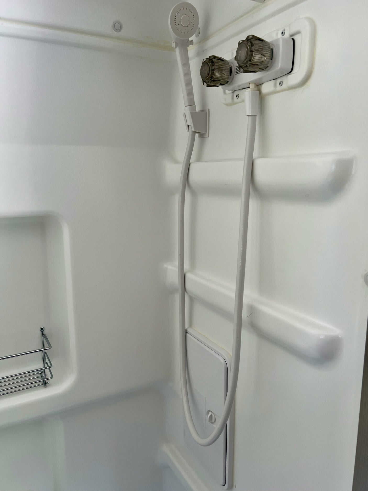 Functional RV rental shower with handheld head, controls, and shelving for a compact space.