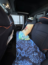 Cozy RV rental back interior with seats folded down, blue blanket, "Happy Camper" pillow, towels, and paper towels for travel.