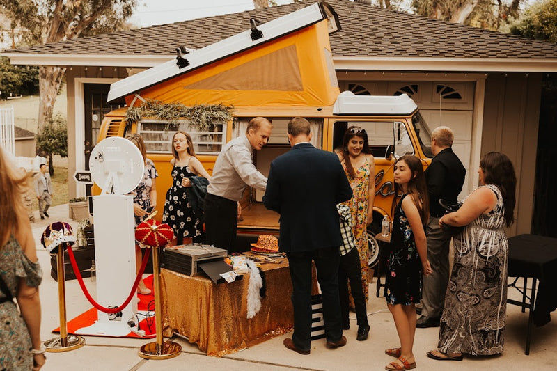 Guests enjoy a vintage orange RV rental camper van photo booth at an outdoor event, complete with fun props. — photo 9