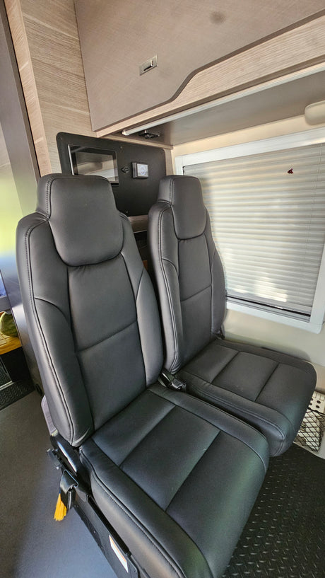 Explore this RV rental's interior. Two comfortable black leather passenger seats, tech control panel, and window with blinds.