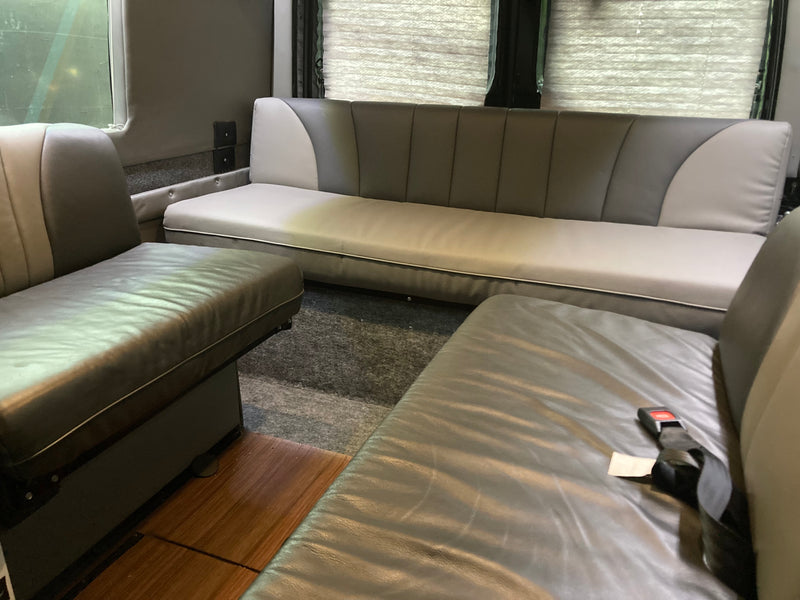 Cozy RV rental interior with comfortable two-tone gray seating, including a long bench and front seats with seatbelts. — photo 15