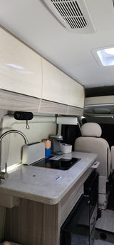 Inside this RV rental, find a compact kitchen: sink, induction cooktop, coffee maker, & overhead cabinets. Ready for adventure.