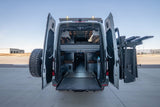 Adventure awaits! This **rv rental** camper van shows its custom interior with a bed, seating, pull-out deck, and rear-mounted gear/tire racks.