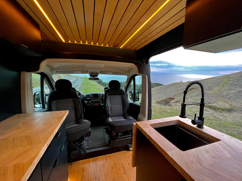 Modern RV rental interior with illuminated wood ceiling, light countertops, sleek black sink, and scenic views. — photo 6