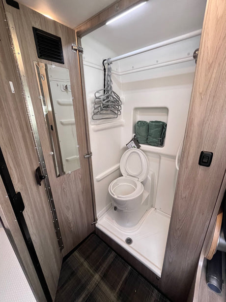 This RV rental's compact wet bath features a toilet, shower with hangers, mirror, and towel storage, maximizing space for travelers.