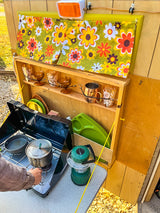 Cooking in a charming RV rental with retro floral curtains, vintage glasses, and a portable camping stove.