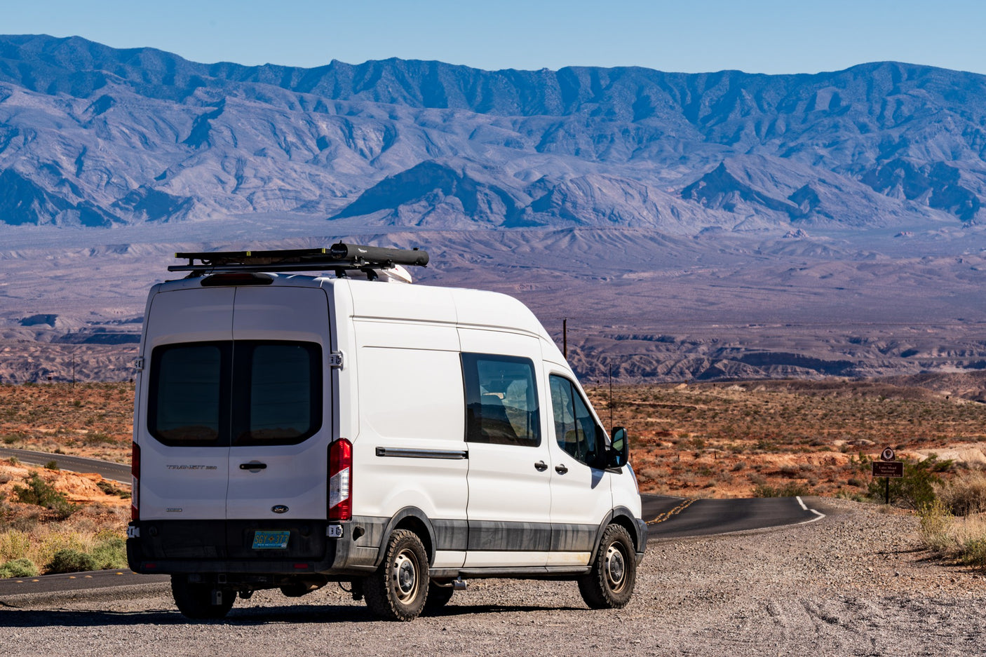 Scenic RV rental: White camper van on a desert road overlooking majestic mountains, ideal for national park exploration.