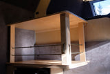 RV rental interior: A wooden shelf unit with elastic cords for secure storage in a campervan.