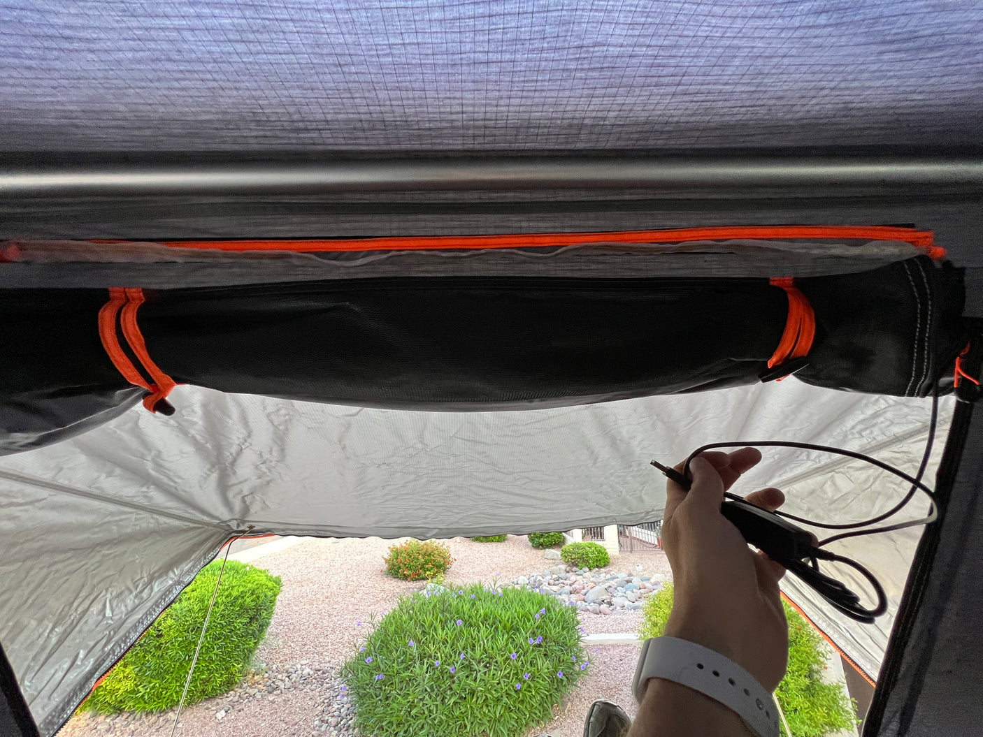 Inside an RV rental tent, a hand holds a power cable, showing the structured interior and outdoor yard view.