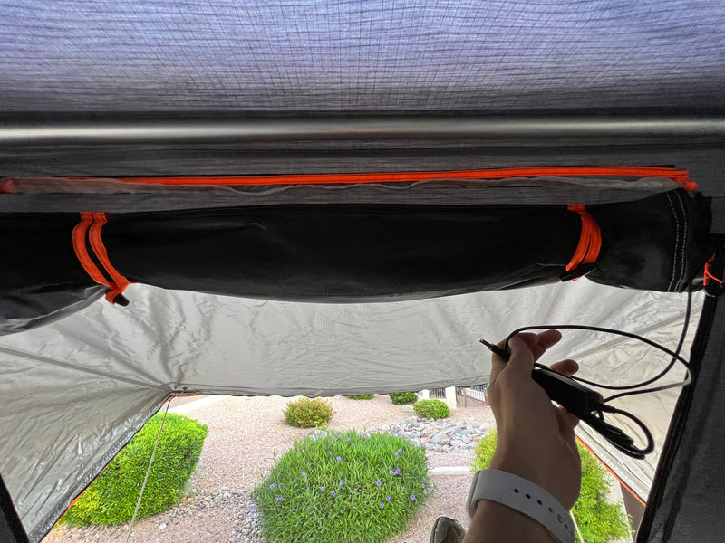 Inside an RV rental tent, a hand holds a power cable, showing the structured interior and outdoor yard view. — photo 12