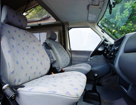 Front interior of an RV rental camper van, showing light patterned seats, dashboard, and a raised pop-top roof.