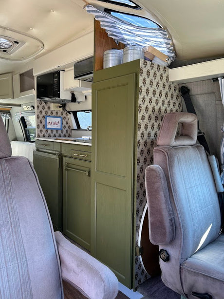 This RV rental interior showcases a charming kitchenette with green cabinets, patterned accents, and comfy front seats.