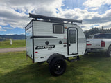 This Sunray Sport rv rental, a compact travel trailer, is ready for adventure, hitched to a truck on a grassy site.